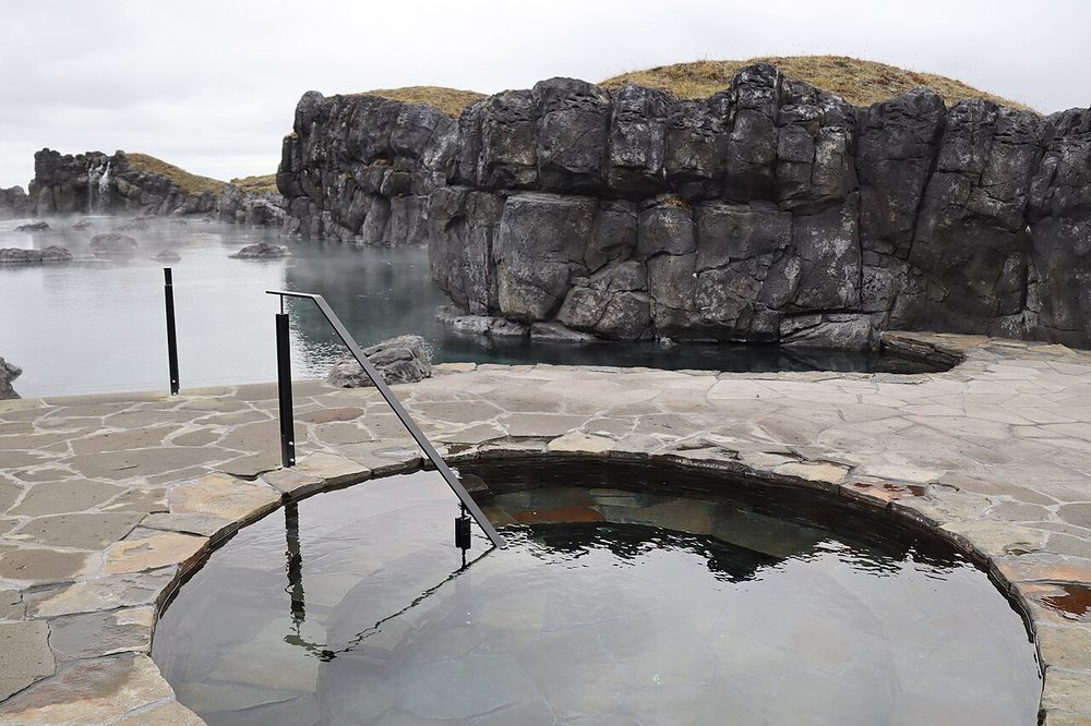 A round stone cold plunge pool with a handrail beside a misty lagoon
